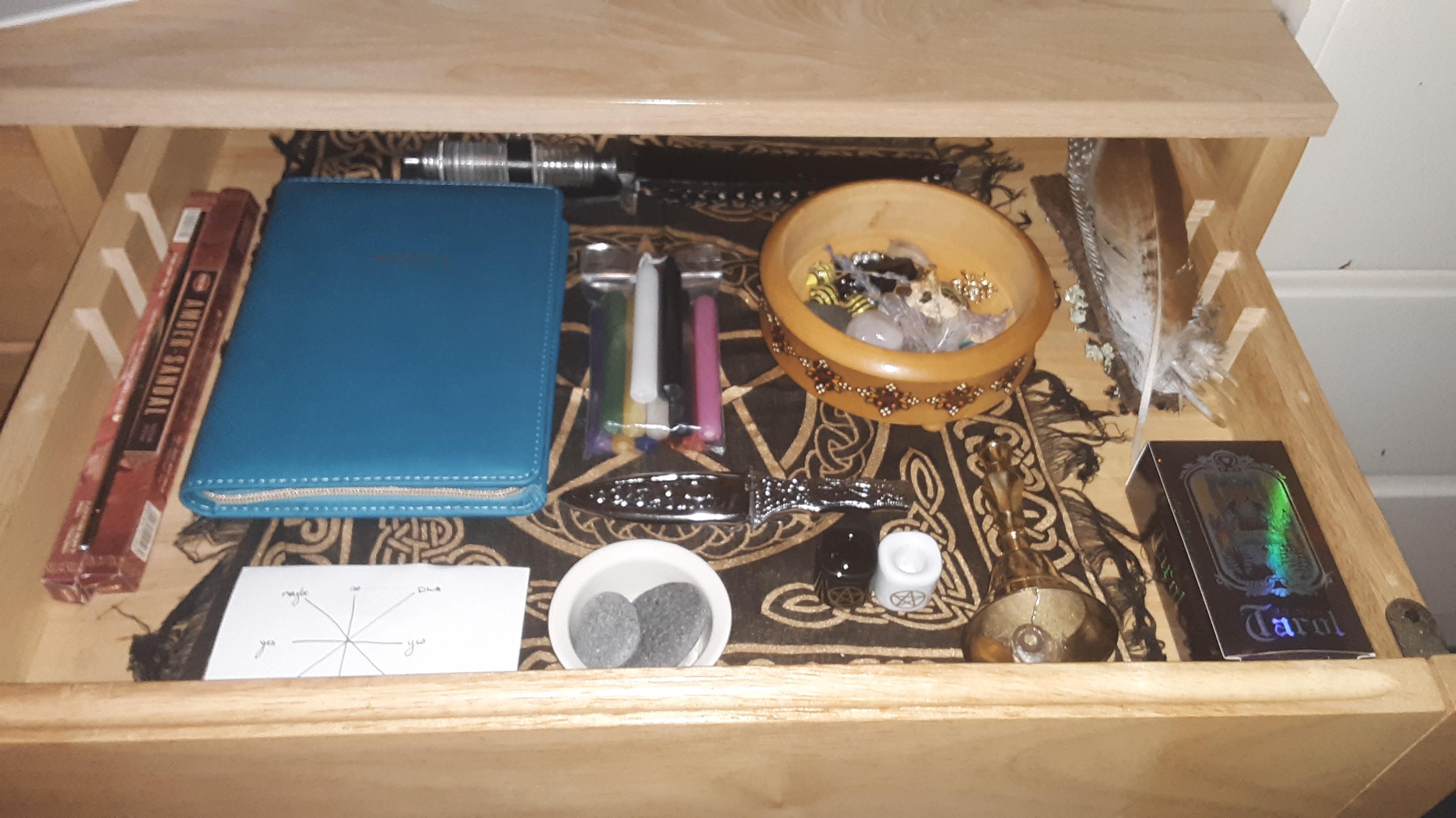 A practice kept in a drawer: journal, candles, blade, bell, stones, and cards.